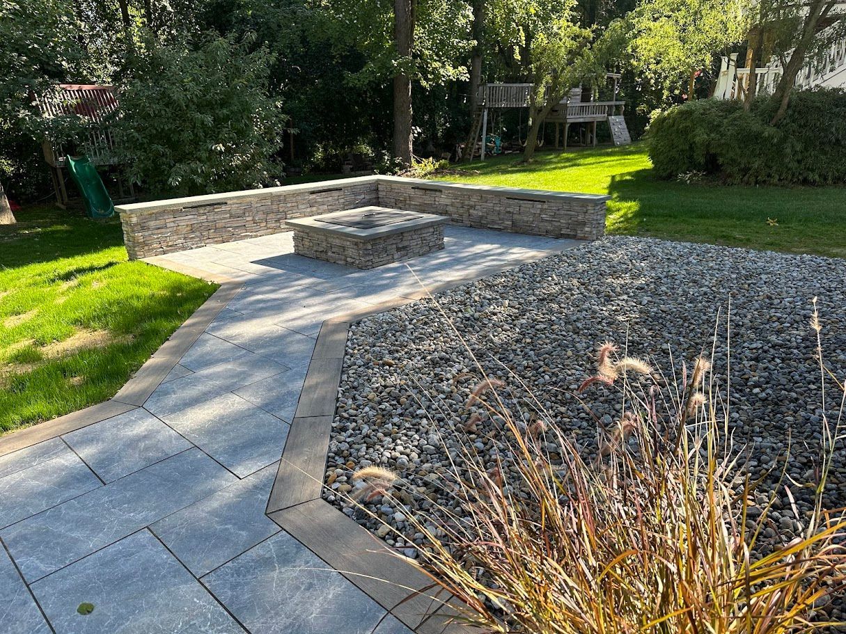 Stone patio with gabion seating and fire pit, surrounded by gravel and grass.