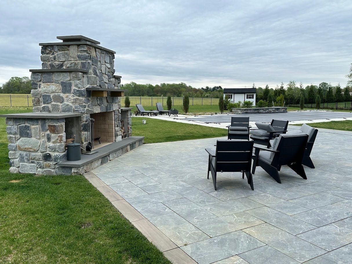 Stone fireplace with seating area overlooking a yard with pool. Overcast sky.