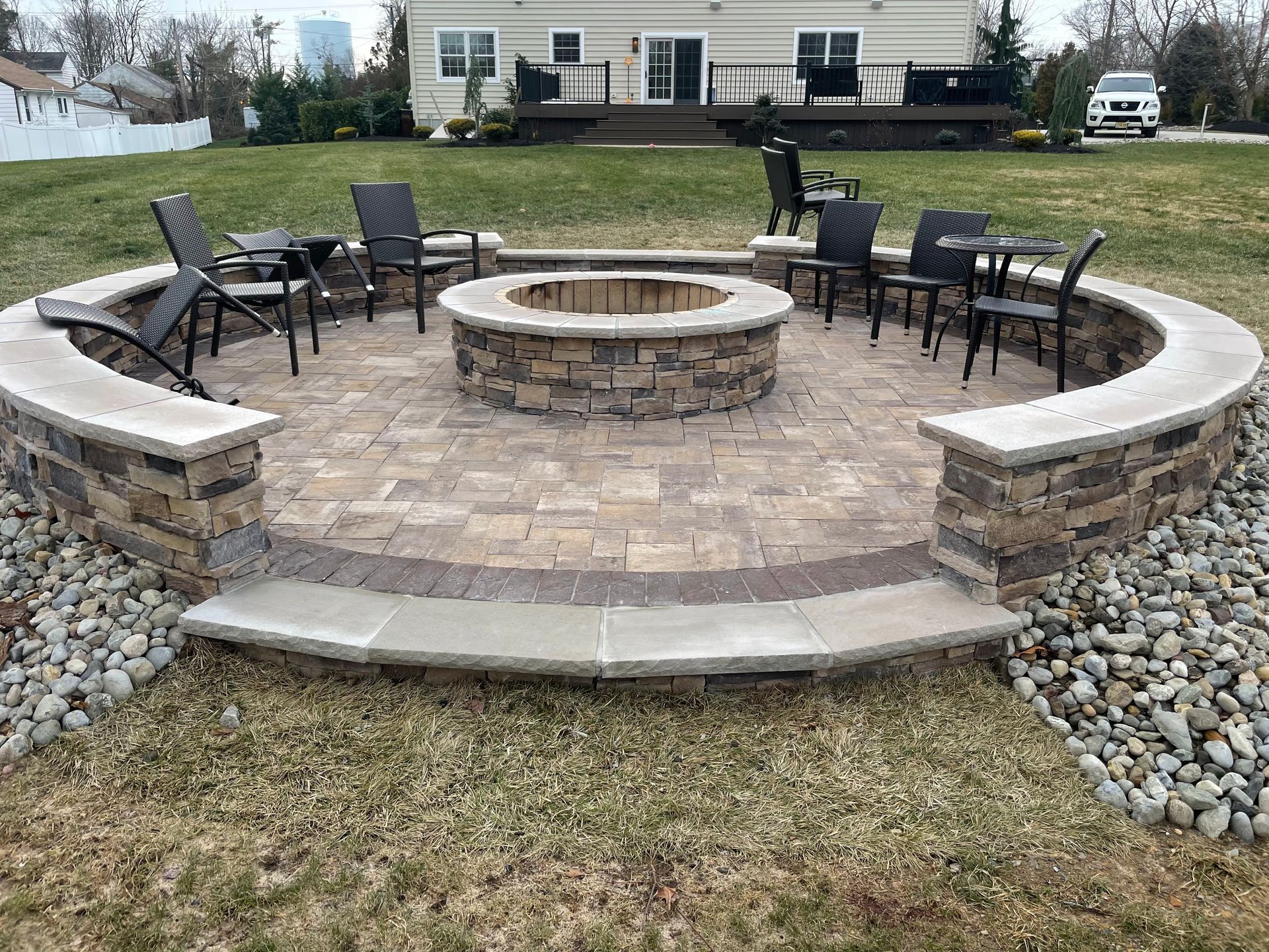 Circular stone fire pit area with seating, surrounded by landscaping, in a backyard.