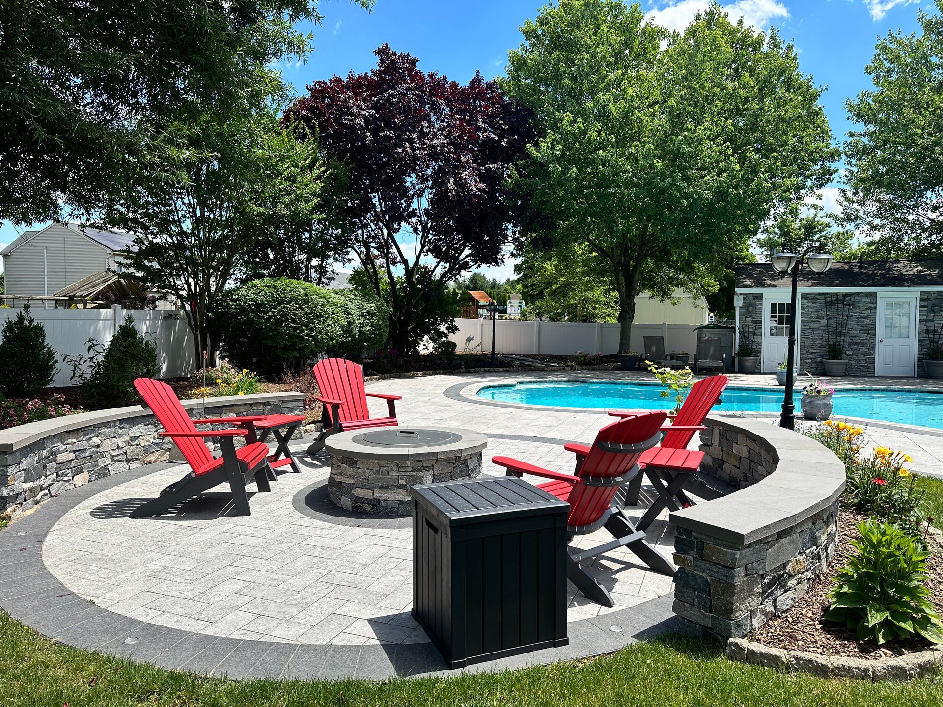 Backyard with a fire pit, red chairs, and a swimming pool surrounded by trees.
