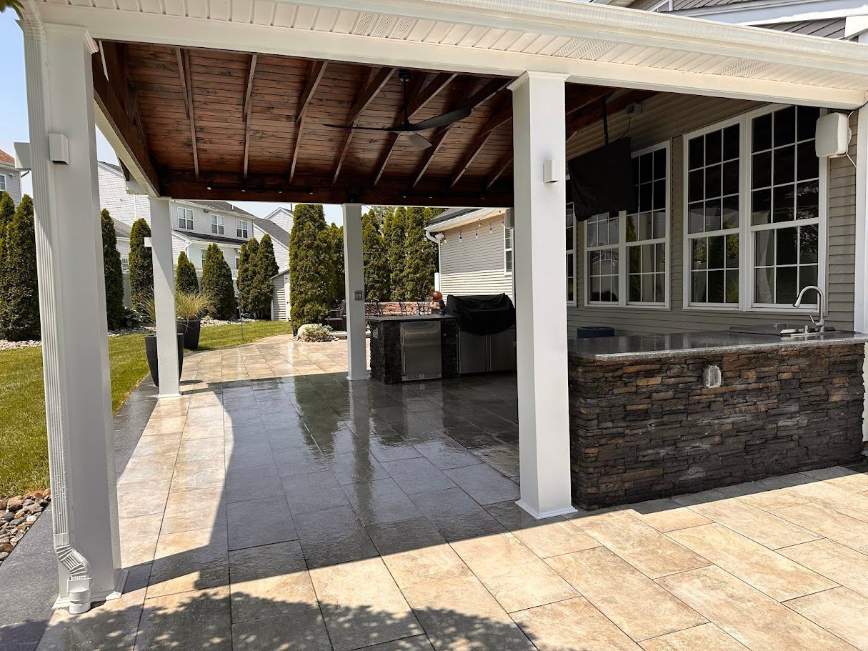 Covered outdoor patio with a wet stone floor, dark wood ceiling, and white columns.