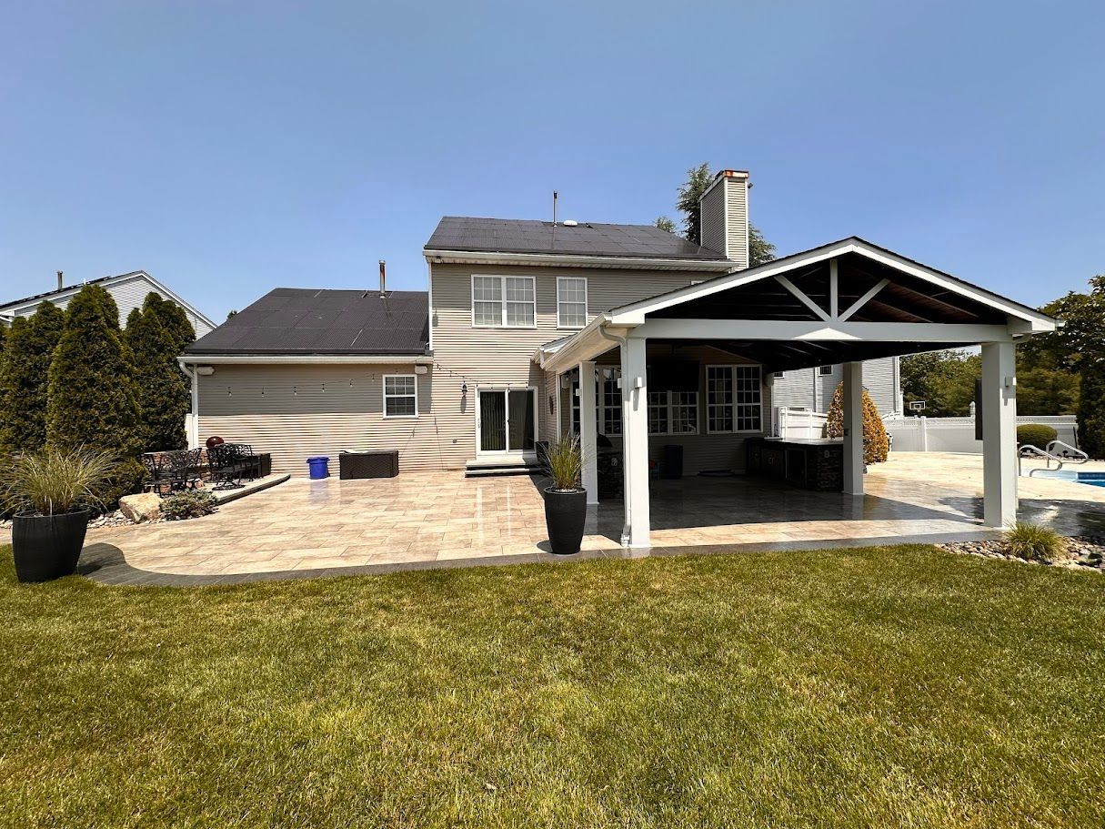 Backyard patio with covered outdoor kitchen, extending from a two-story beige house.