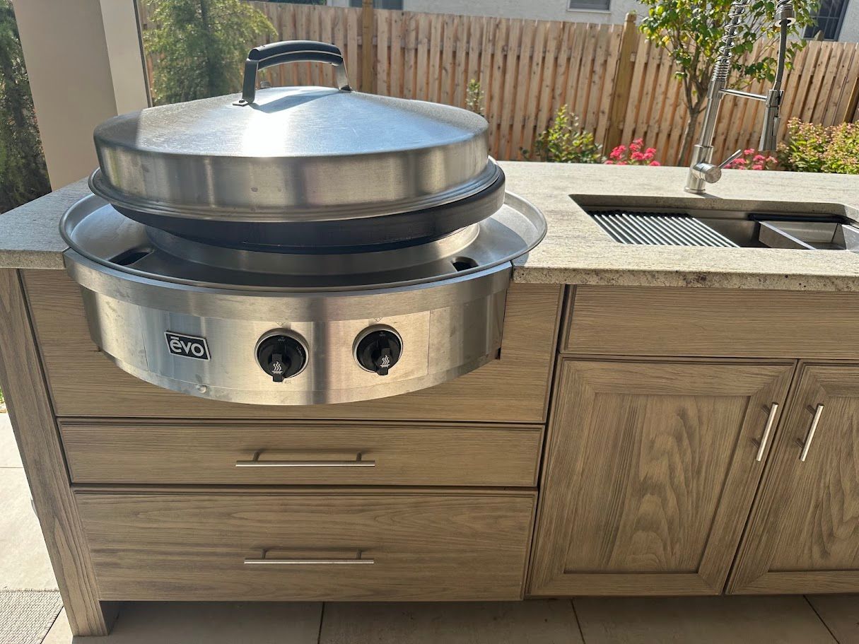 Outdoor grill with stainless steel lid and control knobs, built into a wooden cabinet with a countertop.