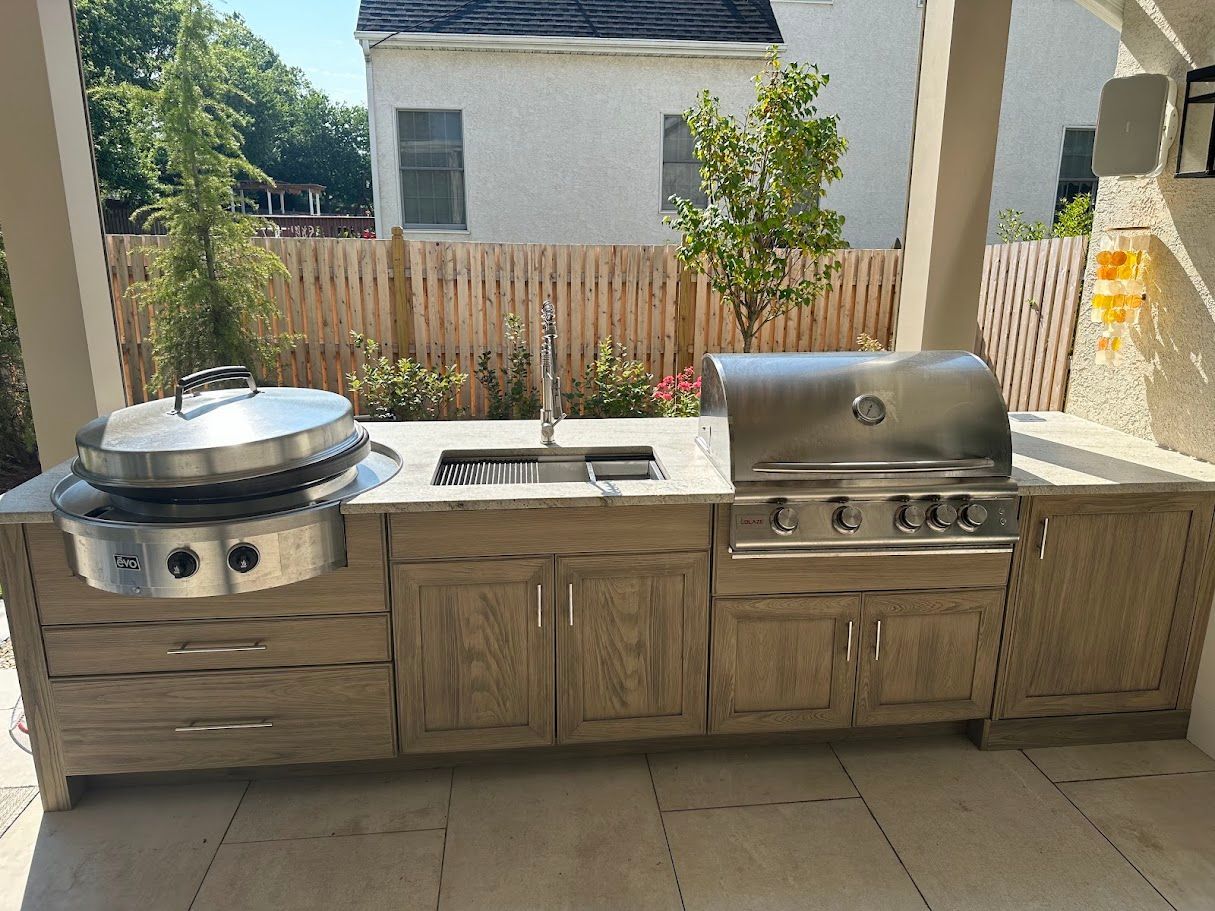 Outdoor kitchen with a grill, sink, and cabinetry on a patio.
