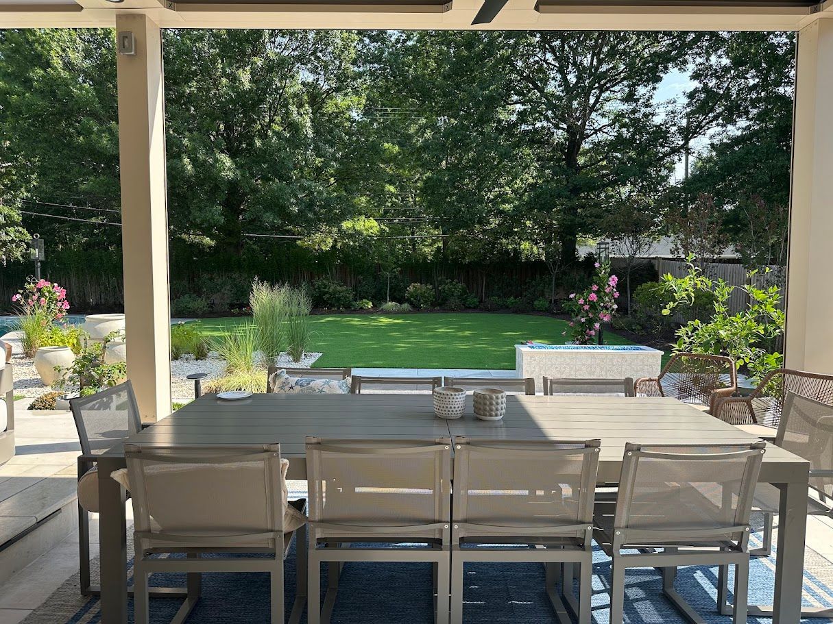 Outdoor dining table and chairs on patio overlooking a green lawn and trees.