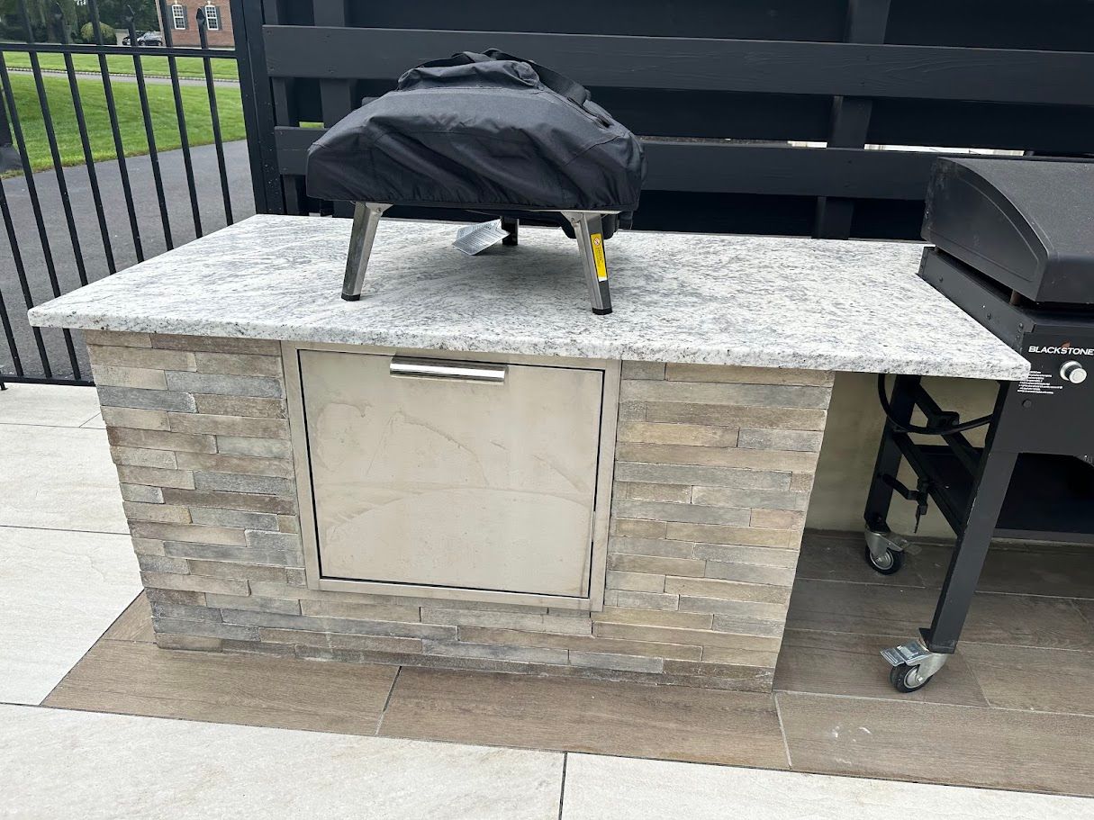 Stone outdoor kitchen island with granite top, cabinet, and grill.