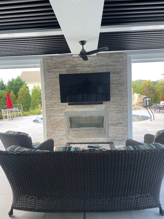 Outdoor living space with TV, fireplace, seating, and a ceiling fan under a pergola.