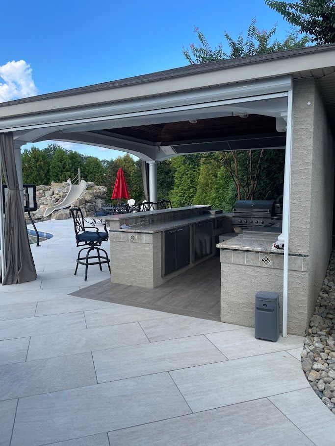 Outdoor kitchen with granite countertops, grill, cabinets, and a bar with seating, beside a pool.