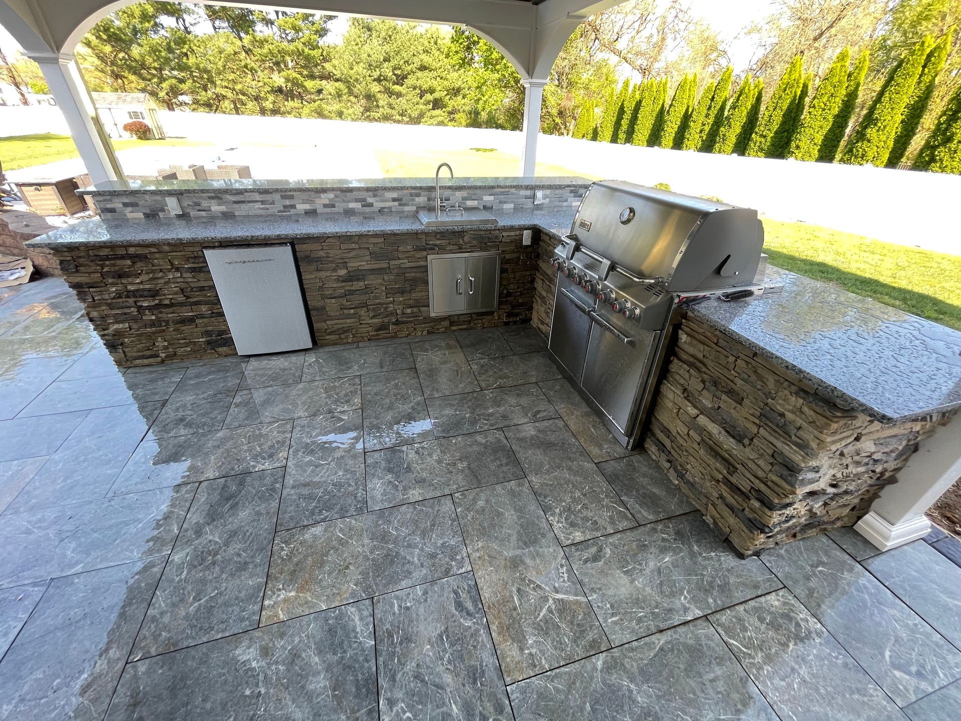 Outdoor kitchen with stone countertop and grill. 