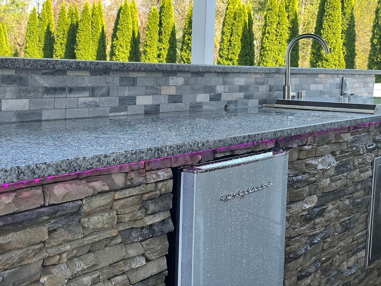 Outdoor kitchen with granite countertop and stone facade, stainless steel sink and appliance.