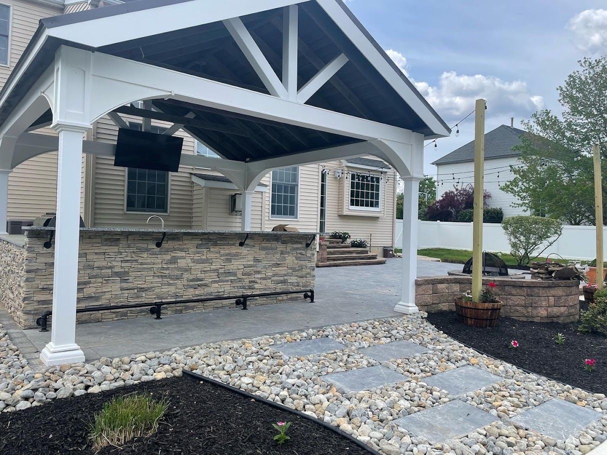 Outdoor kitchen with stone bar, covered seating area, and paved pathway.