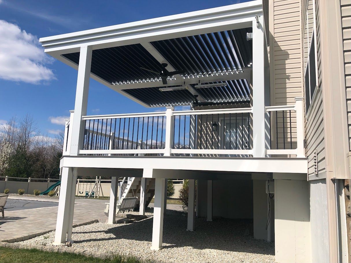 White elevated deck with pergola and black louvers, attached to a house.