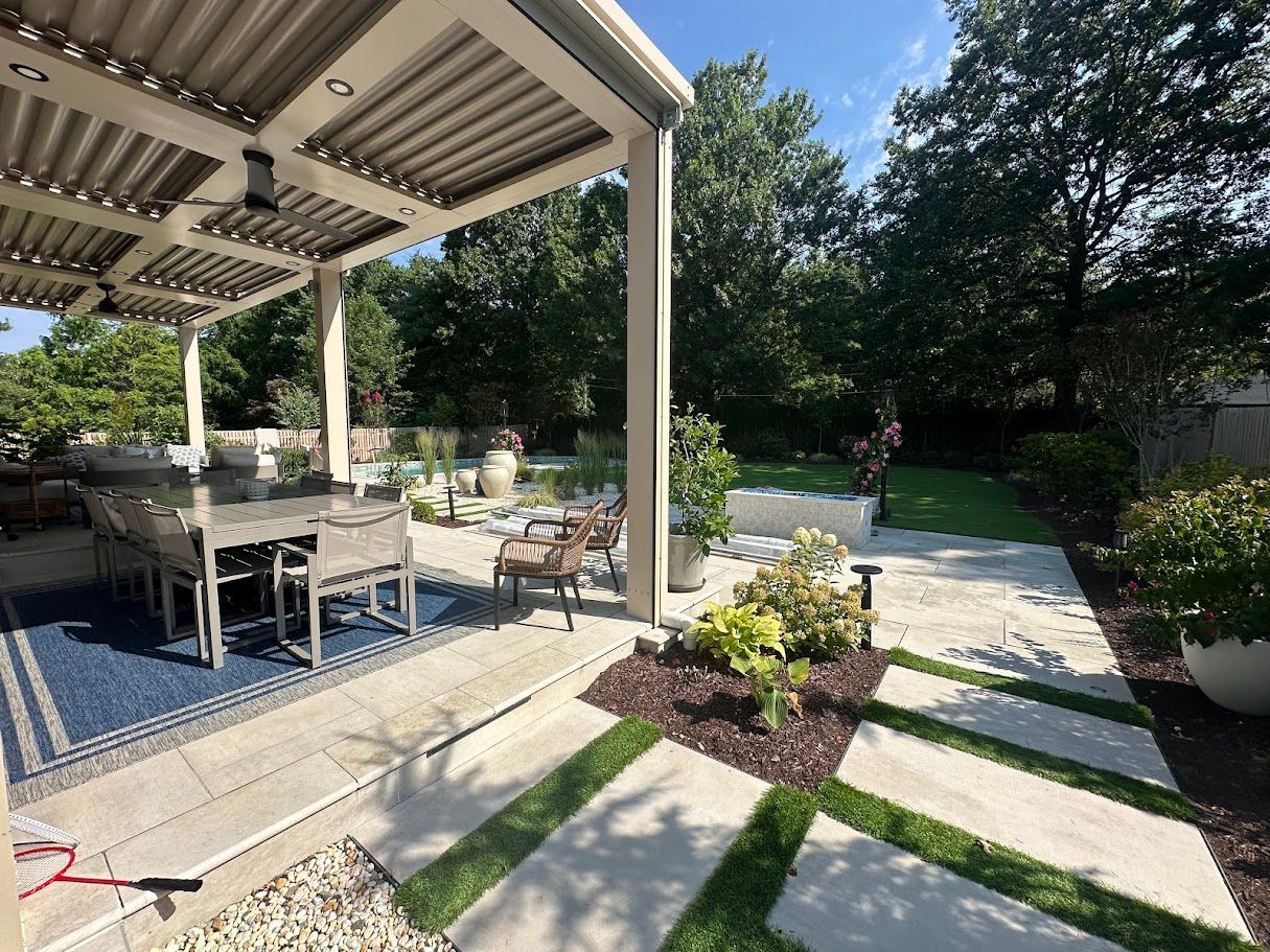 Outdoor patio with dining table under a pergola, lush greenery, and stepping stone path.