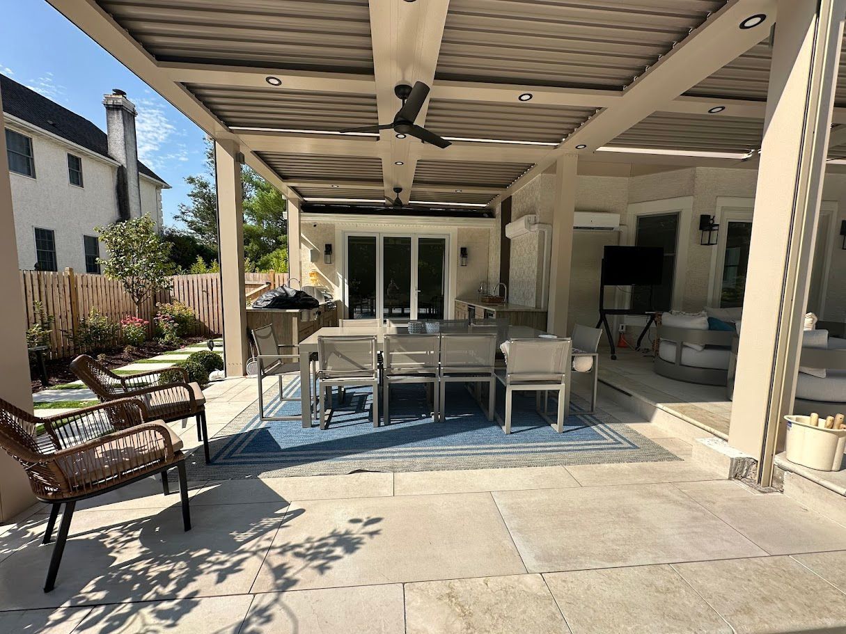 Patio with dining table, seating, and pergola. Blue rug on concrete. Beige and brown tones.