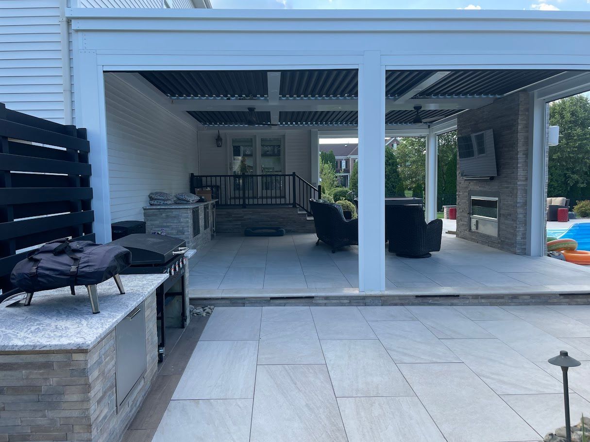 Outdoor patio with kitchen, seating area, and TV under a white pergola.
