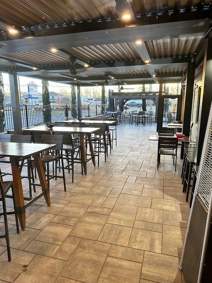 Outdoor patio with tables and chairs under a pergola roof, view toward other tables and buildings.