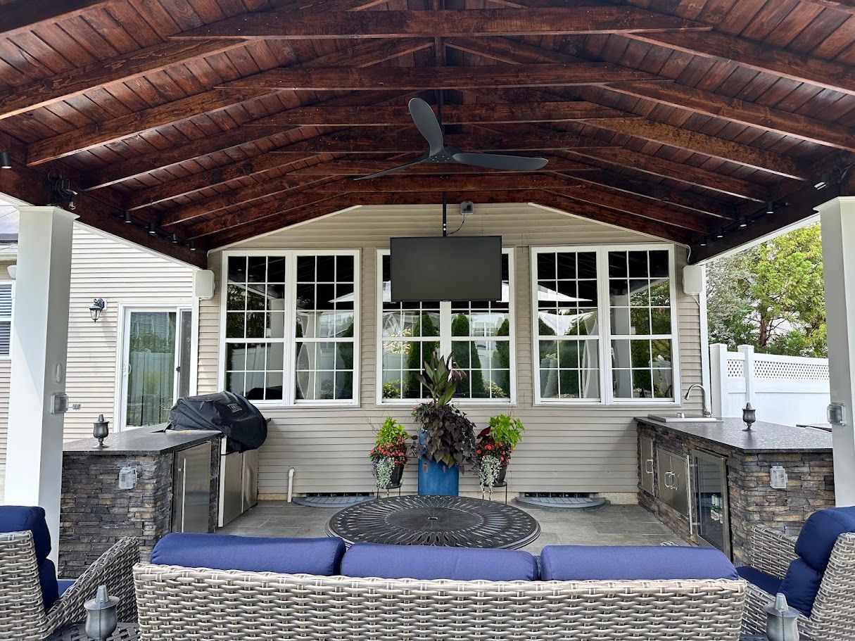 Covered outdoor patio with a TV, couches, and a grill.