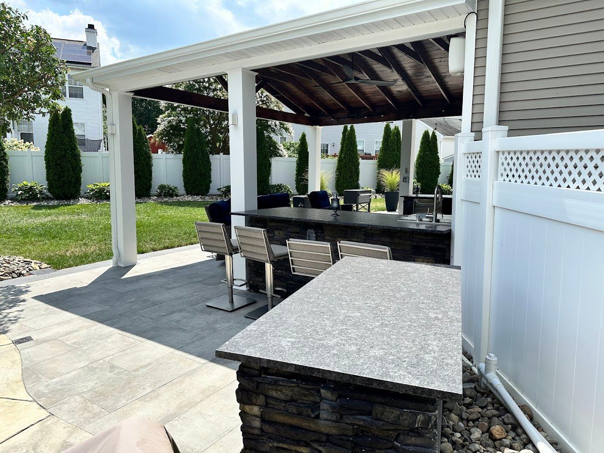 Outdoor kitchen with a bar, seating, and a covered cooking area; backyard setting.