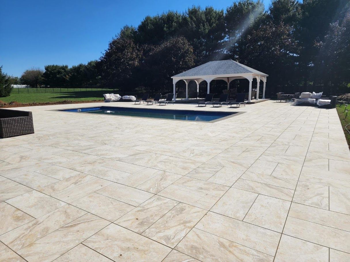 Pool and gazebo in a sunny outdoor setting with light-colored paving.