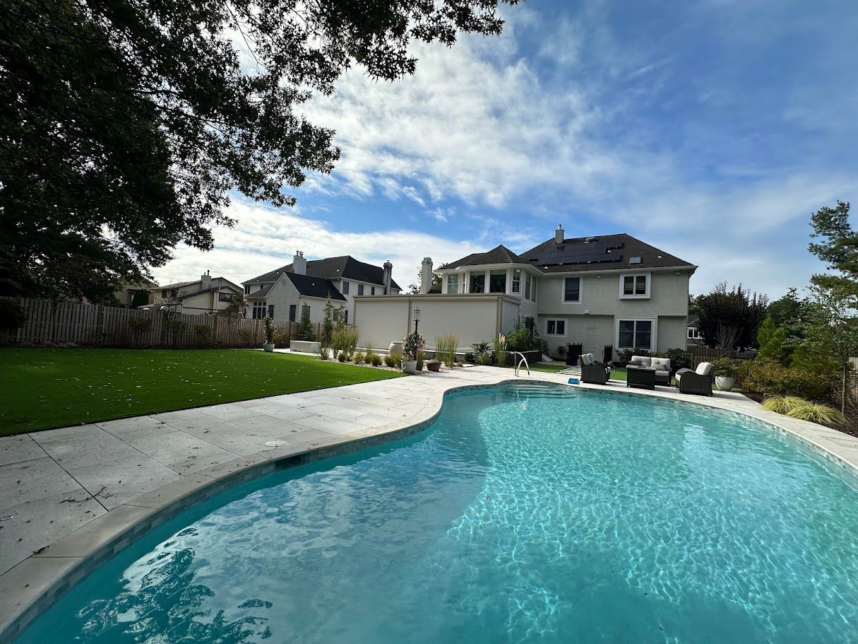 Backyard with a pool, house, green grass, and blue sky.
