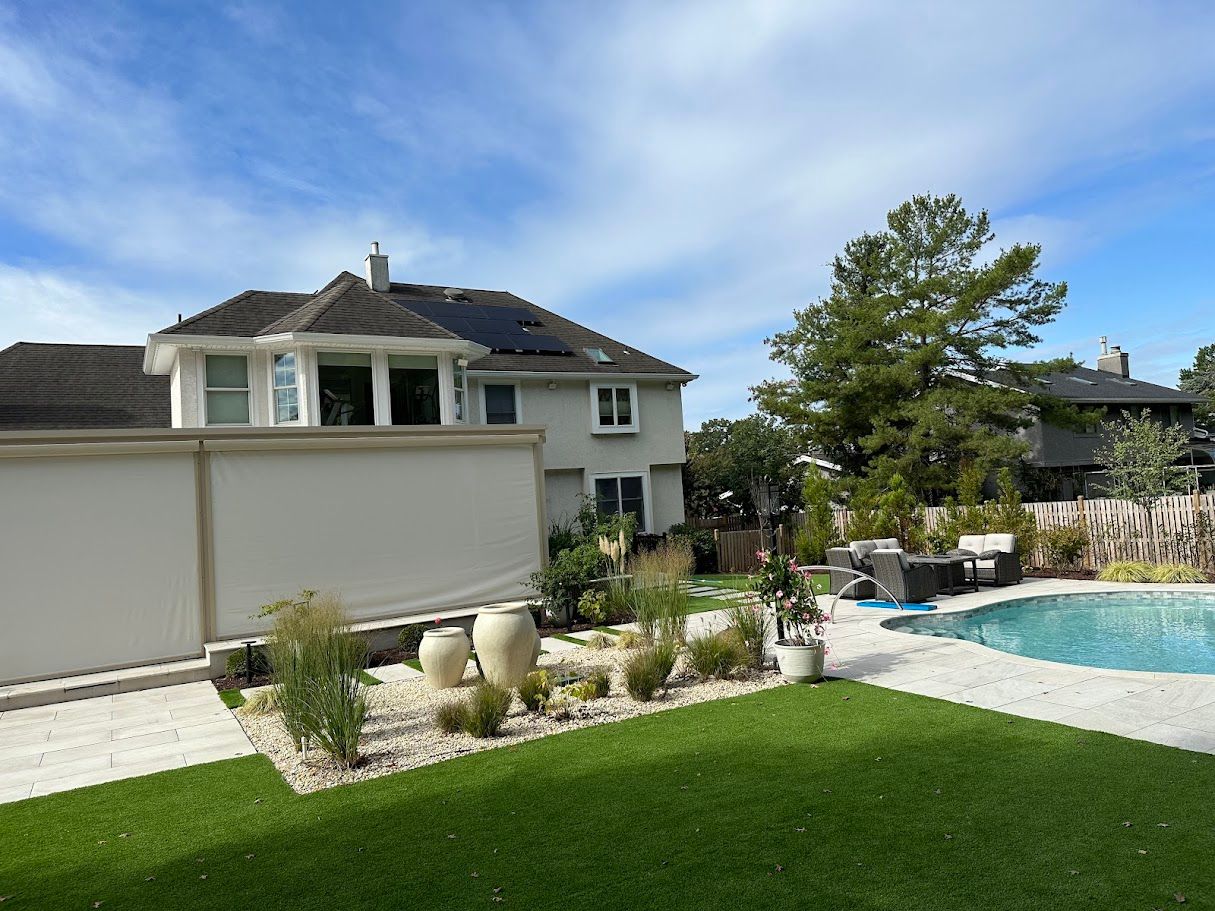 Backyard with a house, pool, and landscaping. Bright green lawn, blue sky, and white walls.