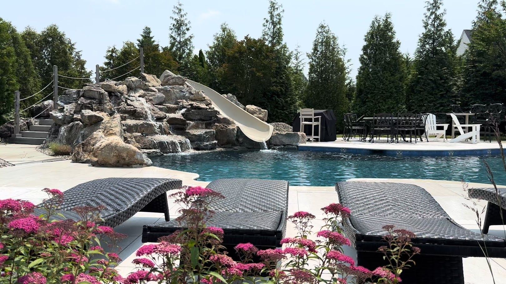 Swimming pool with waterfall feature, slide, and lounge chairs.