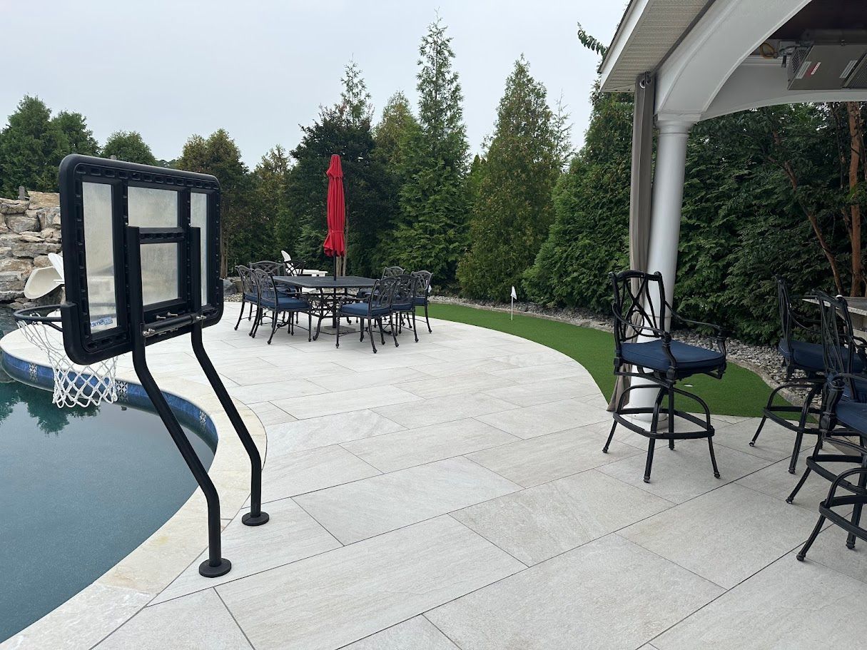 Outdoor patio with swimming pool, basketball hoop, tables, chairs, and lush greenery.
