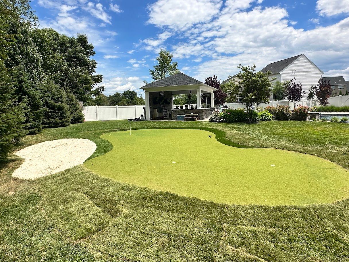 Backyard with a putting green, sand trap, and gazebo under a blue sky.