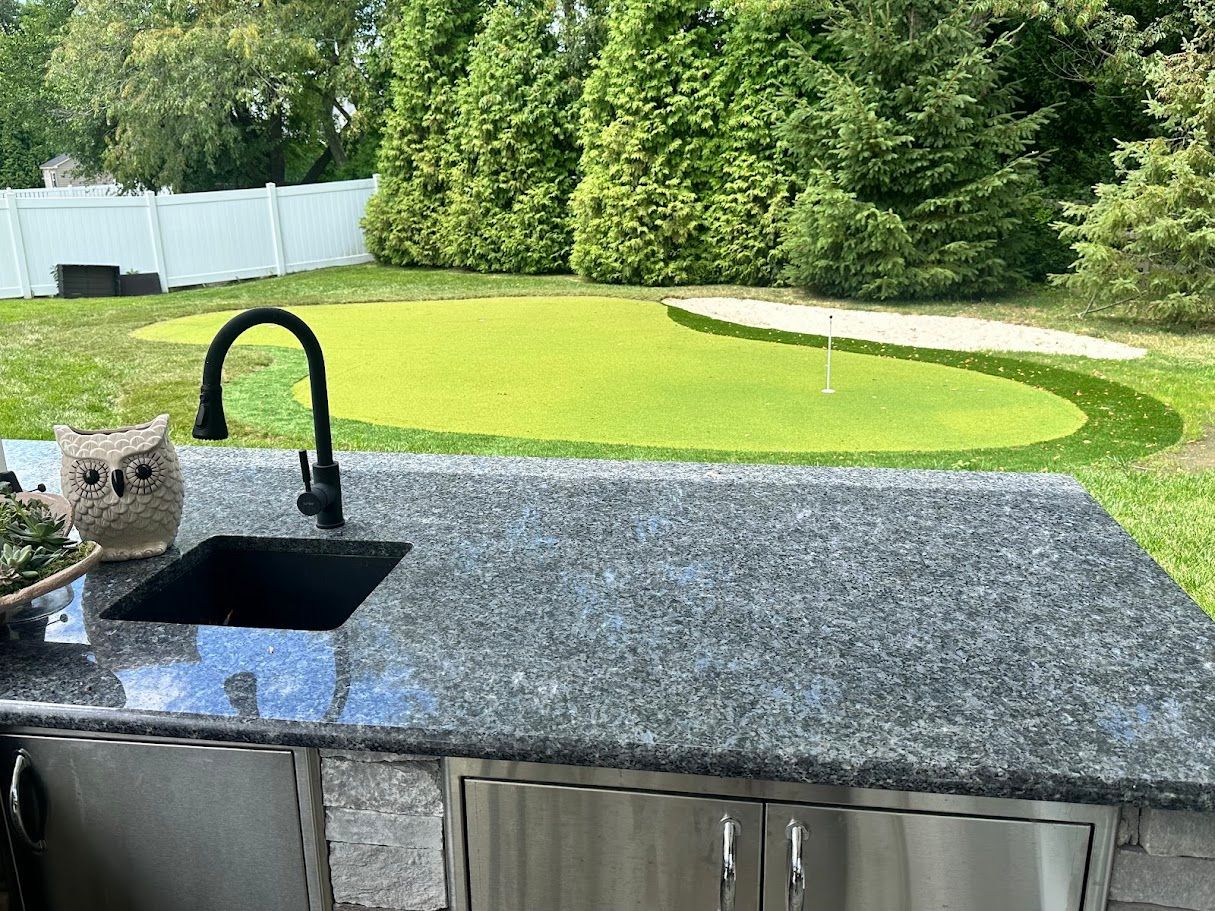 Outdoor kitchen with granite countertop and a putting green in the background.