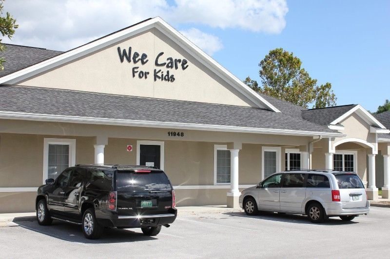 Two cars are parked in front of a building that says wee care for kids