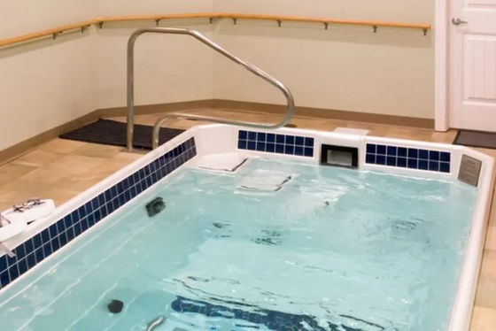 Indoor spa pool with blue water, metal handrail, and bench seating along the wall