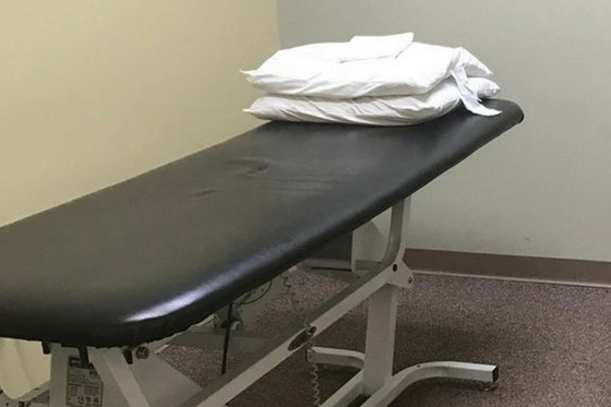 Examination table with folded white sheets in a small medical room