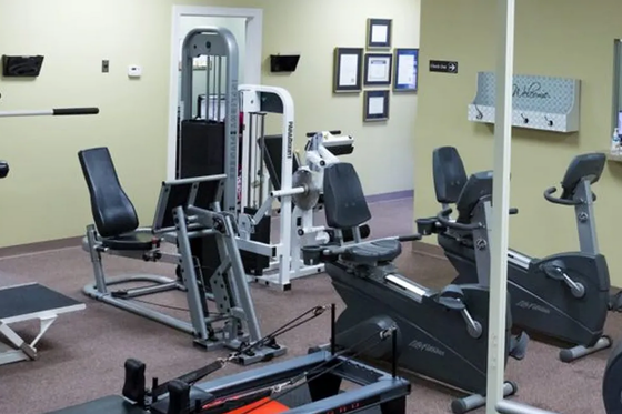 Gym room with exercise machines, black chairs, and wall mirrors in a beige-walled fitness area