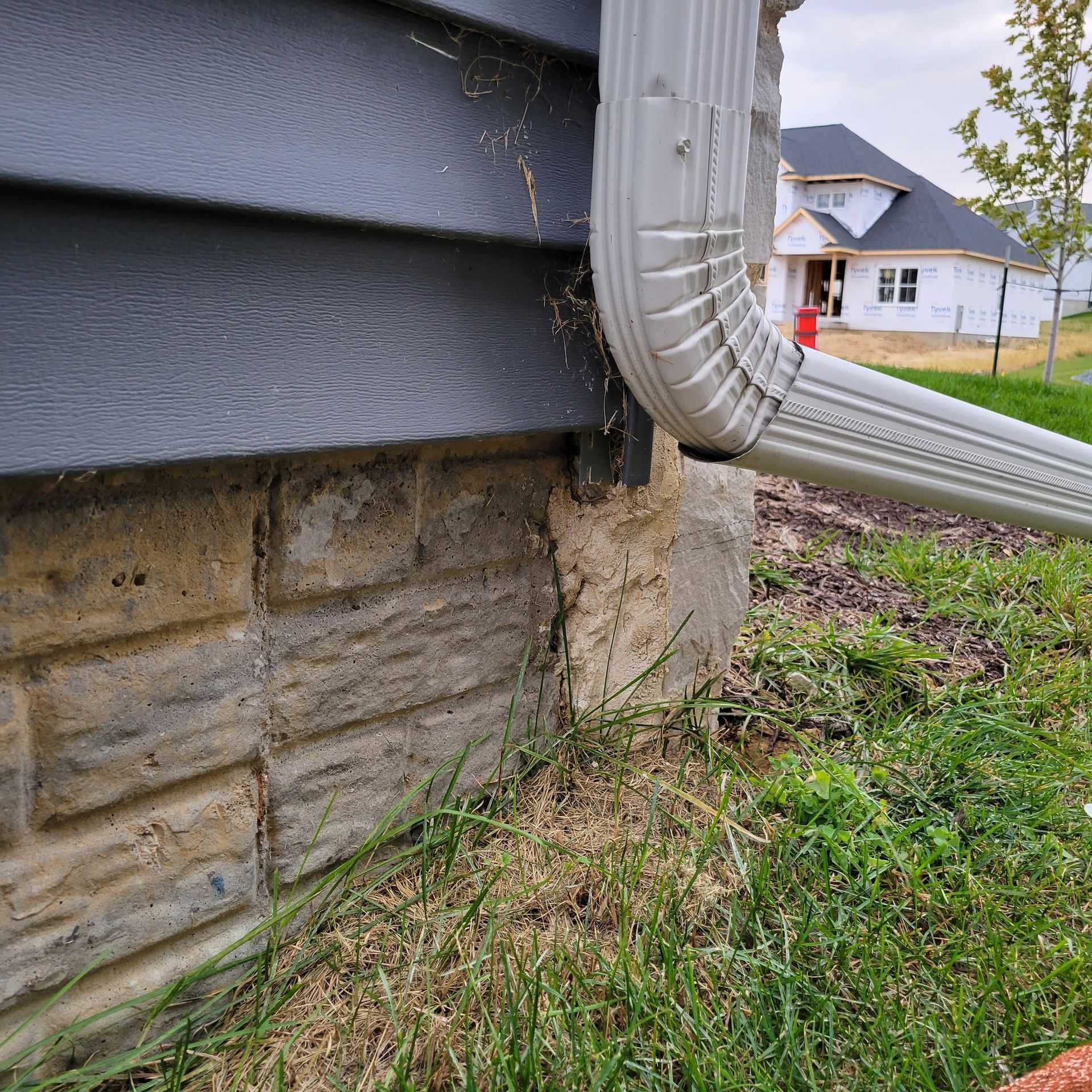 Corner of a house with gray siding and stone foundation, gray gutter, and green grass.