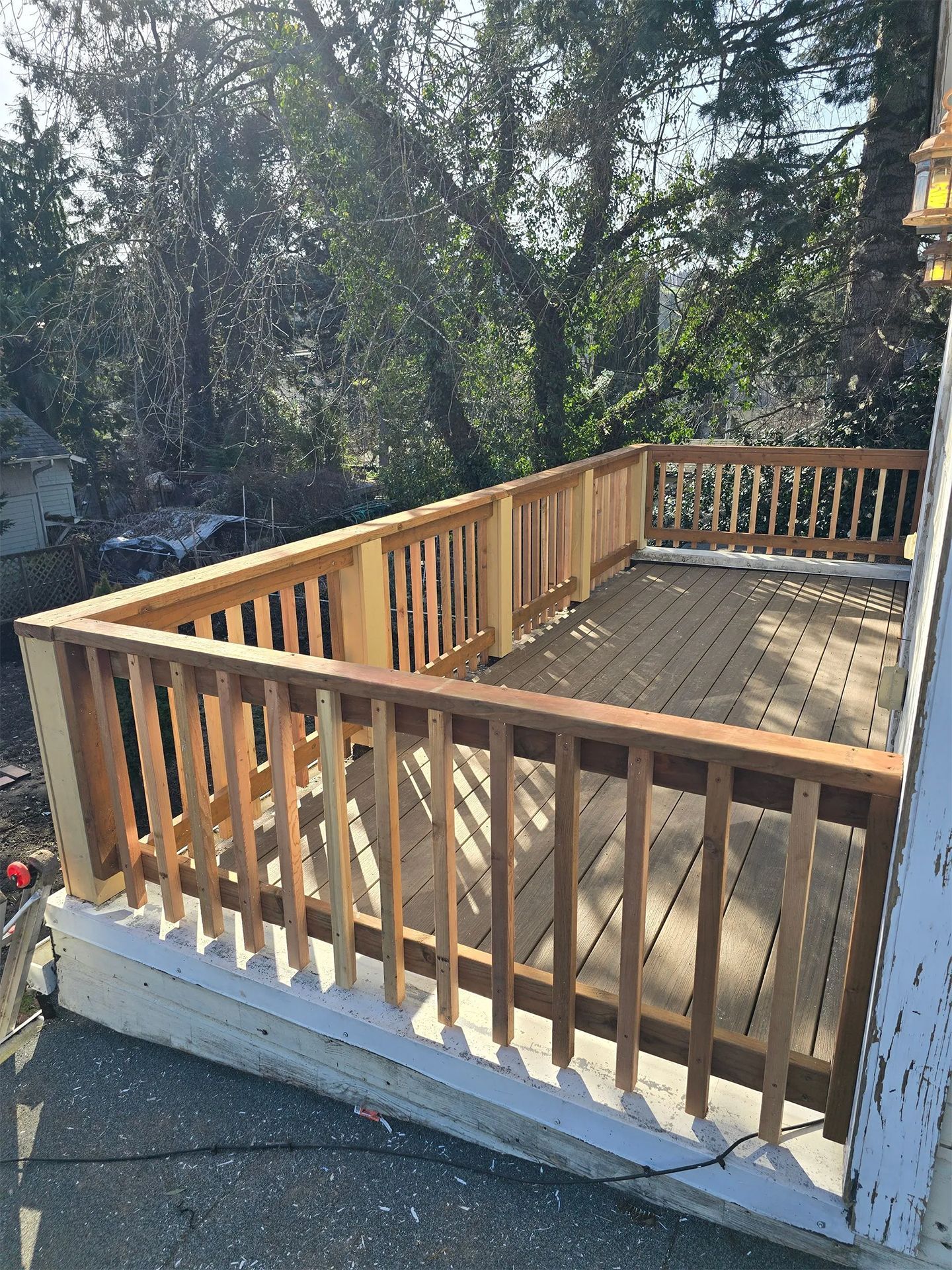Wooden deck with railing, constructed on a concrete base. Sunlight illuminates the structure surrounded by trees.