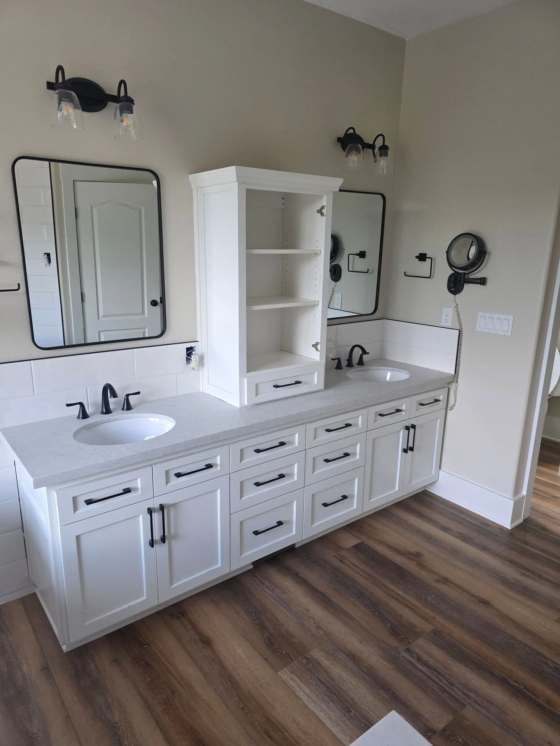 Bathroom with white double vanity, mirrors, and storage cabinet; brown wood-look floor.