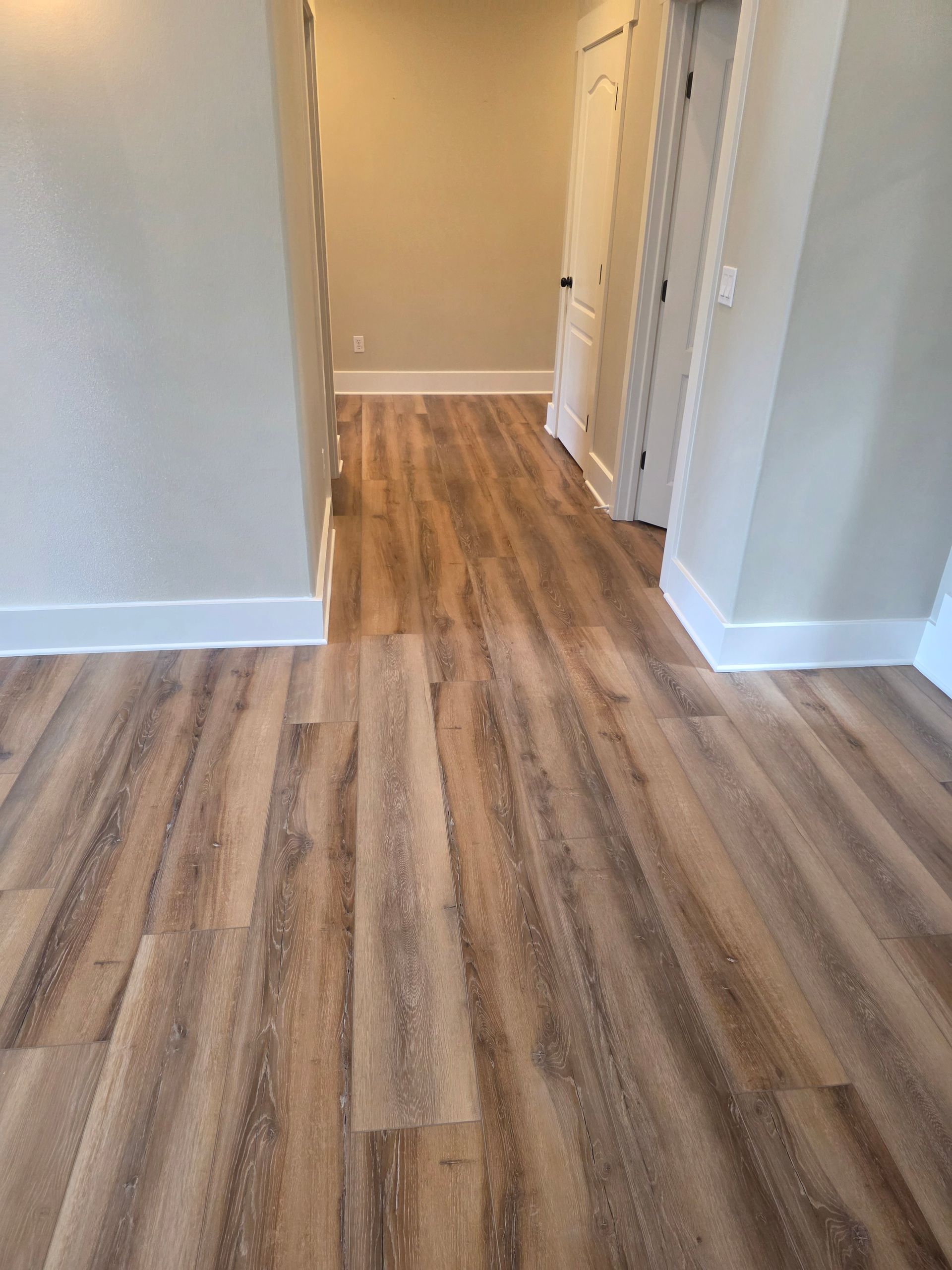 Wooden floor hallway with white trim, leading to a doorway and two other doors.