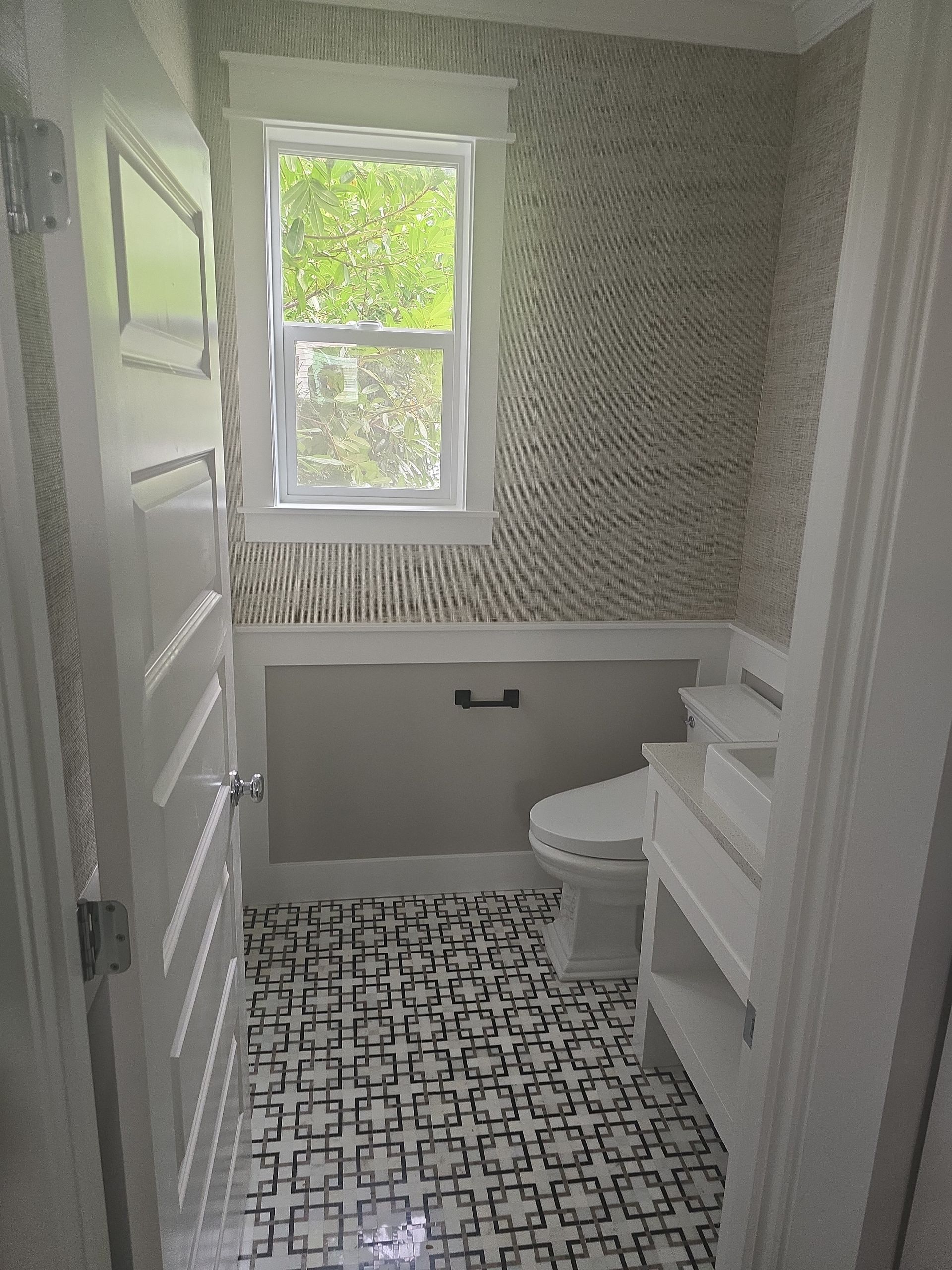 Small bathroom with patterned floor, wallpaper, toilet, and window with natural light.