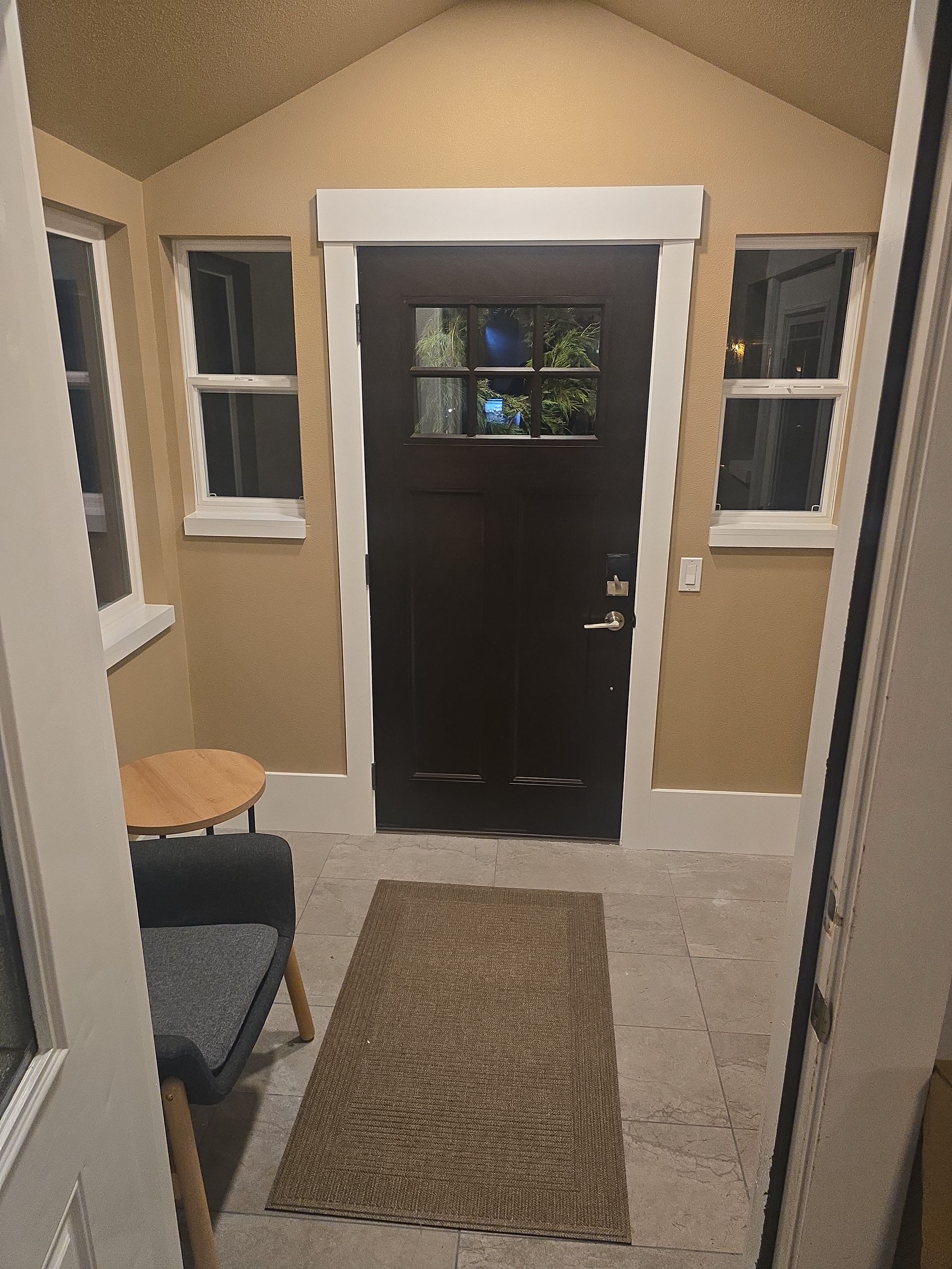 Small entryway with dark door, rug, two windows, and small chair; beige walls.