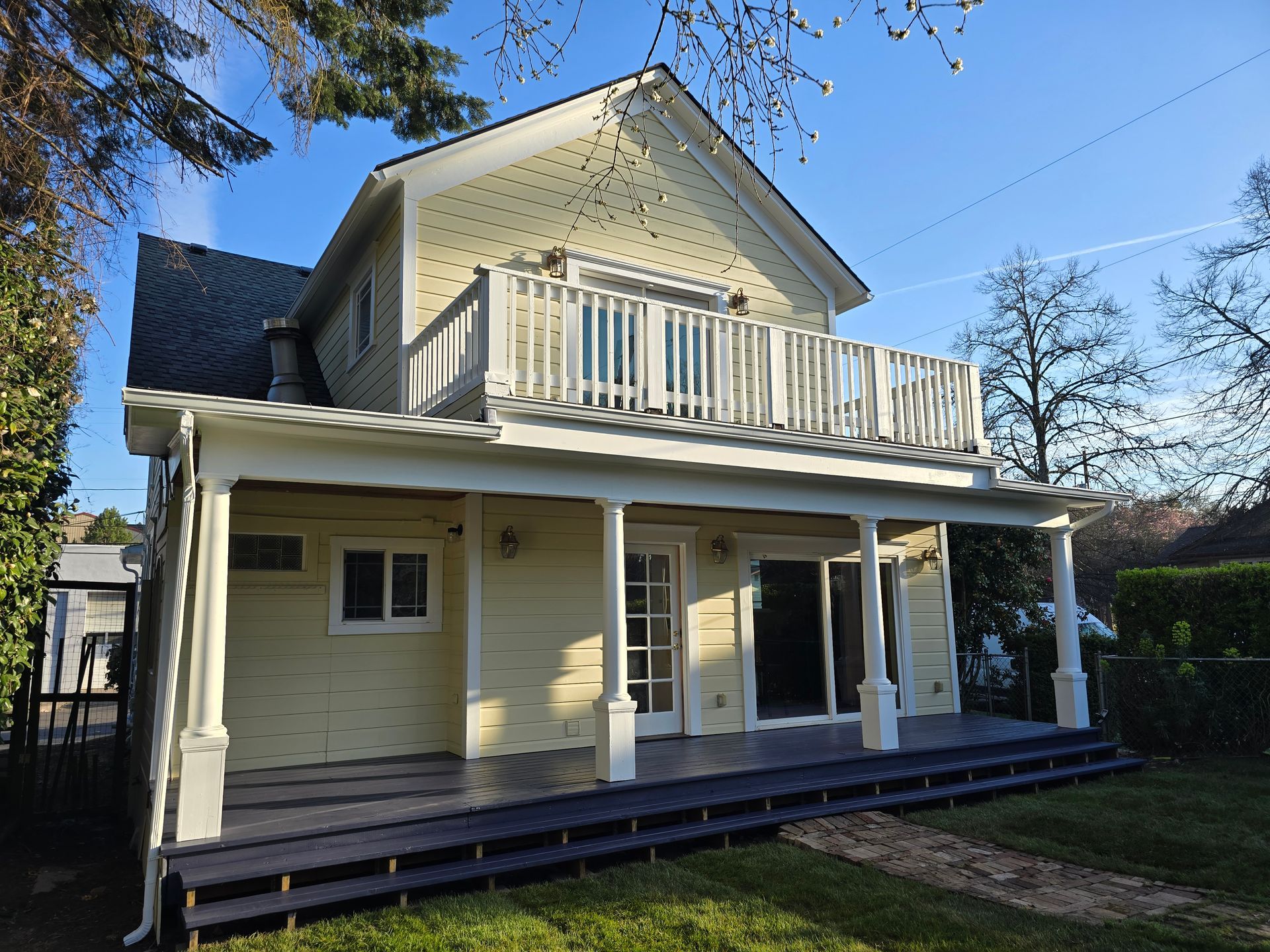 Yellow two-story house with white porch and balcony; sunny day.