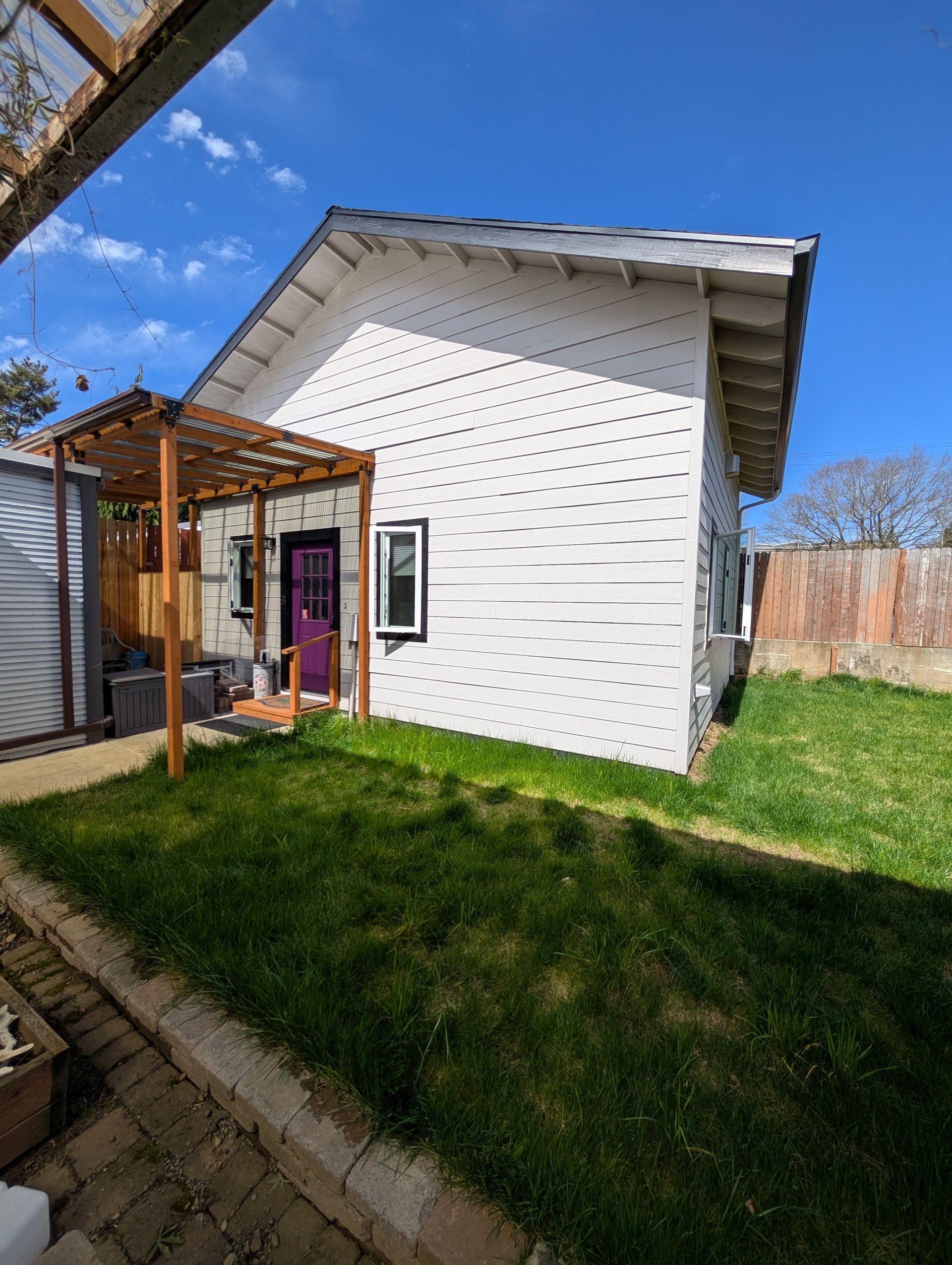 Small white house exterior with a wooden porch, red door, and green lawn on a sunny day