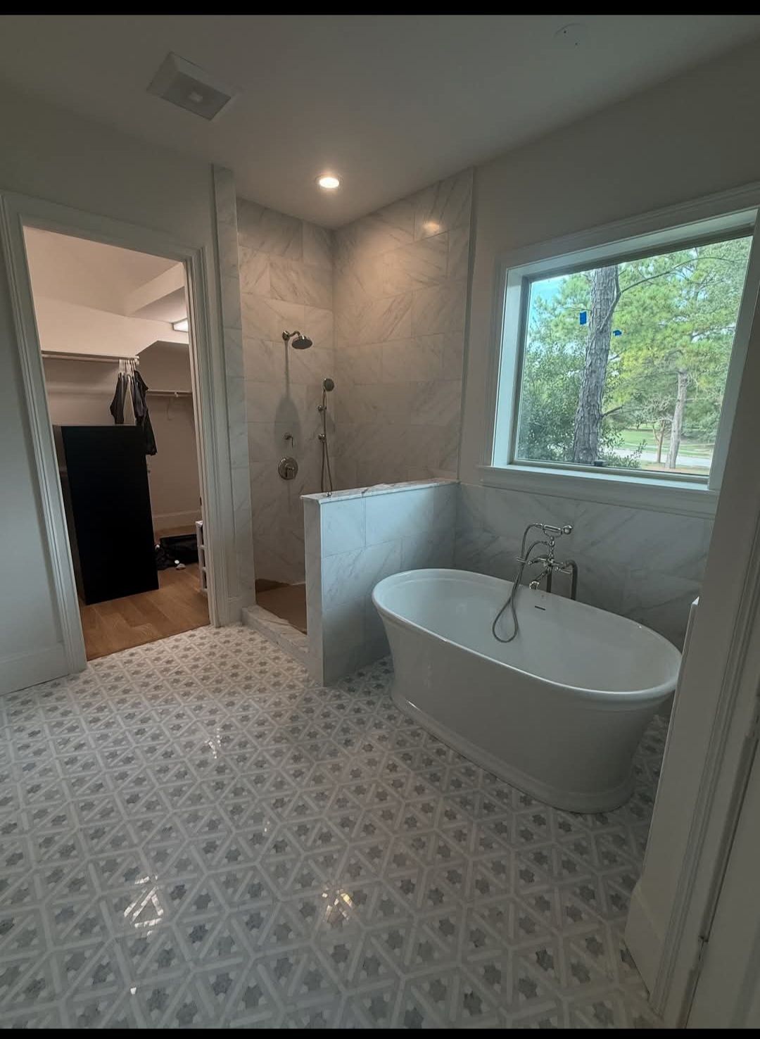 Bright tiled bathroom with freestanding tub, walk-in shower, and large window overlooking trees