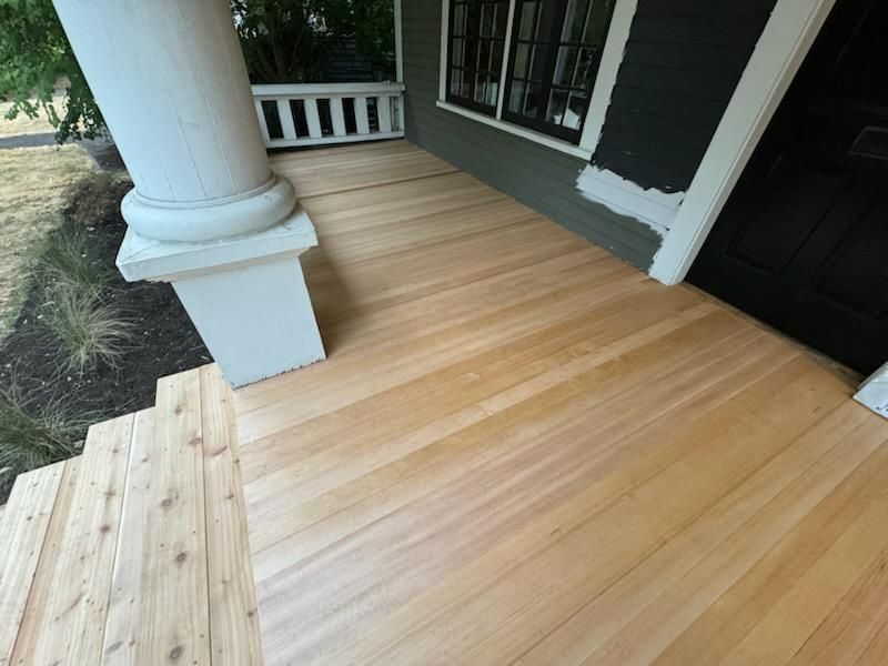 Wooden front porch with white column, steps, and black front door on a house exterior