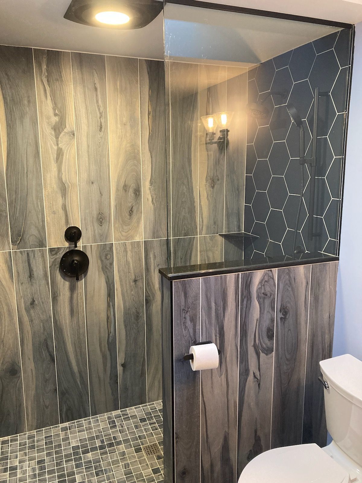 Modern bathroom shower with wood-look walls, dark accent tile, and mosaic floor.