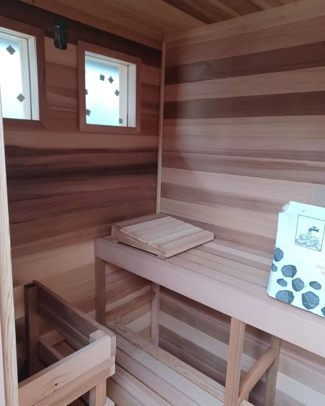 Wood-paneled sauna interior with benches, small windows, and folded towels