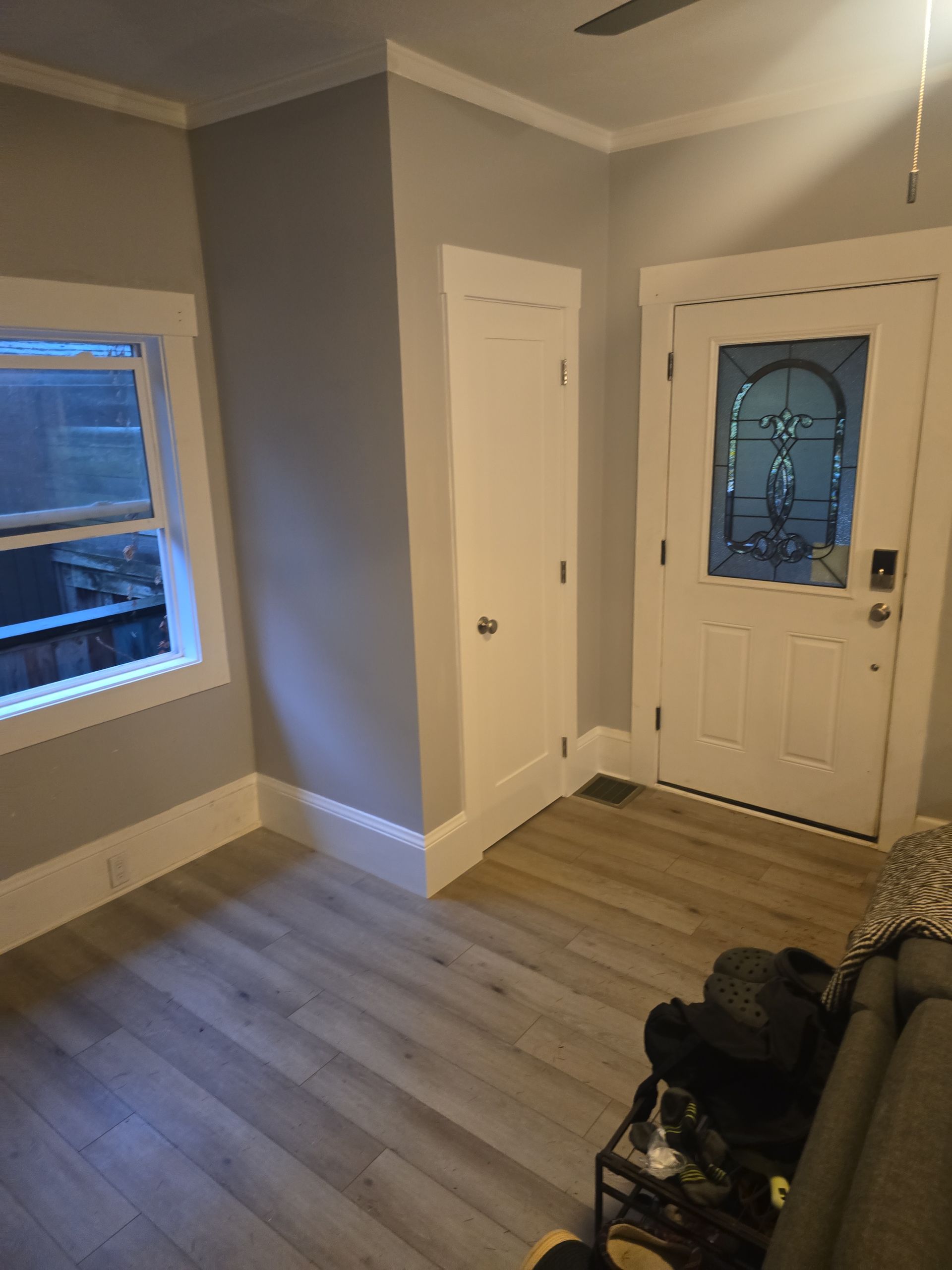 Small entryway with white front door, gray walls, wood floor, and a window seat by the window.