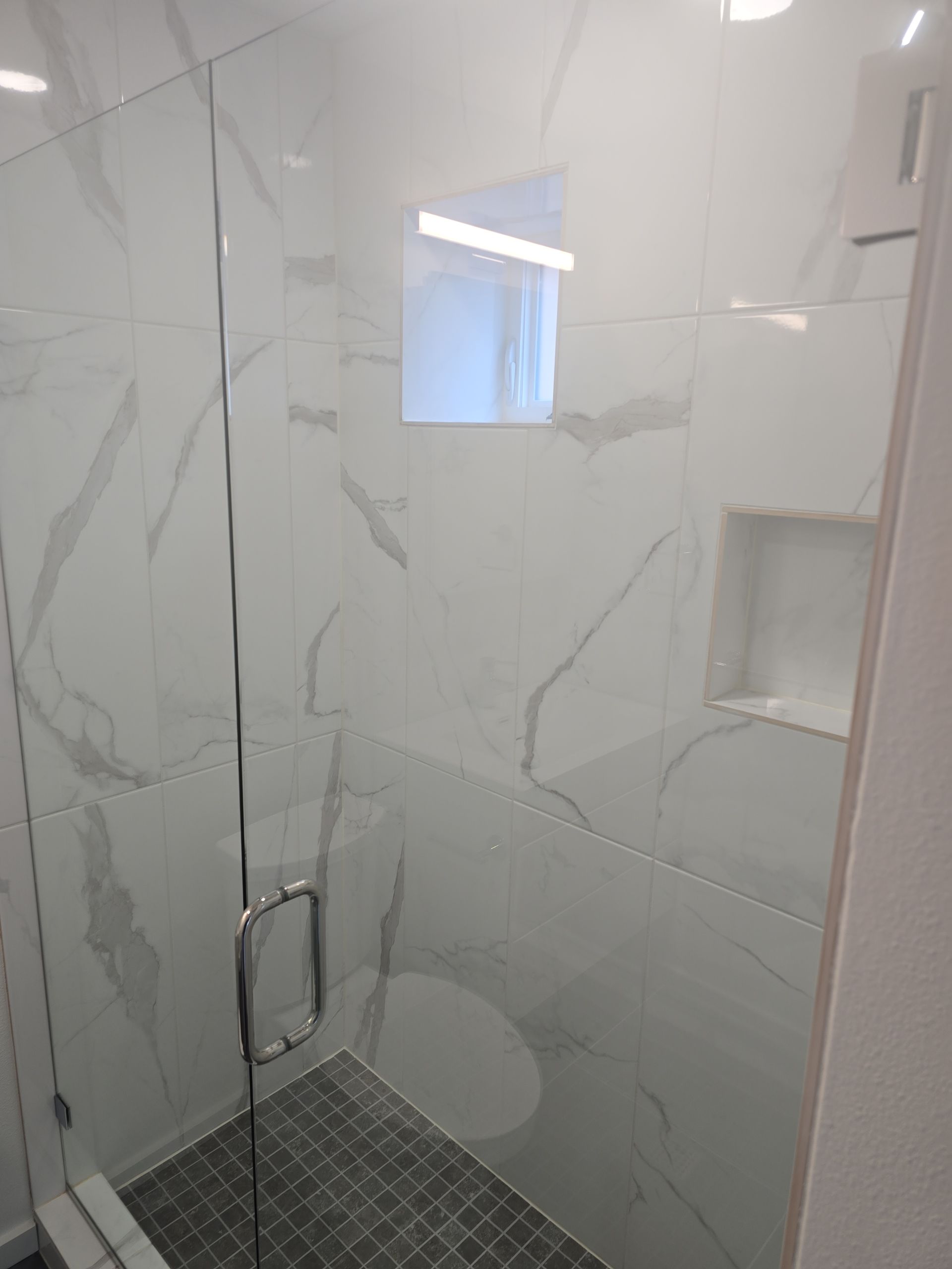 Modern shower with marble-look tile, gray mosaic floor, glass door, and built-in niche.