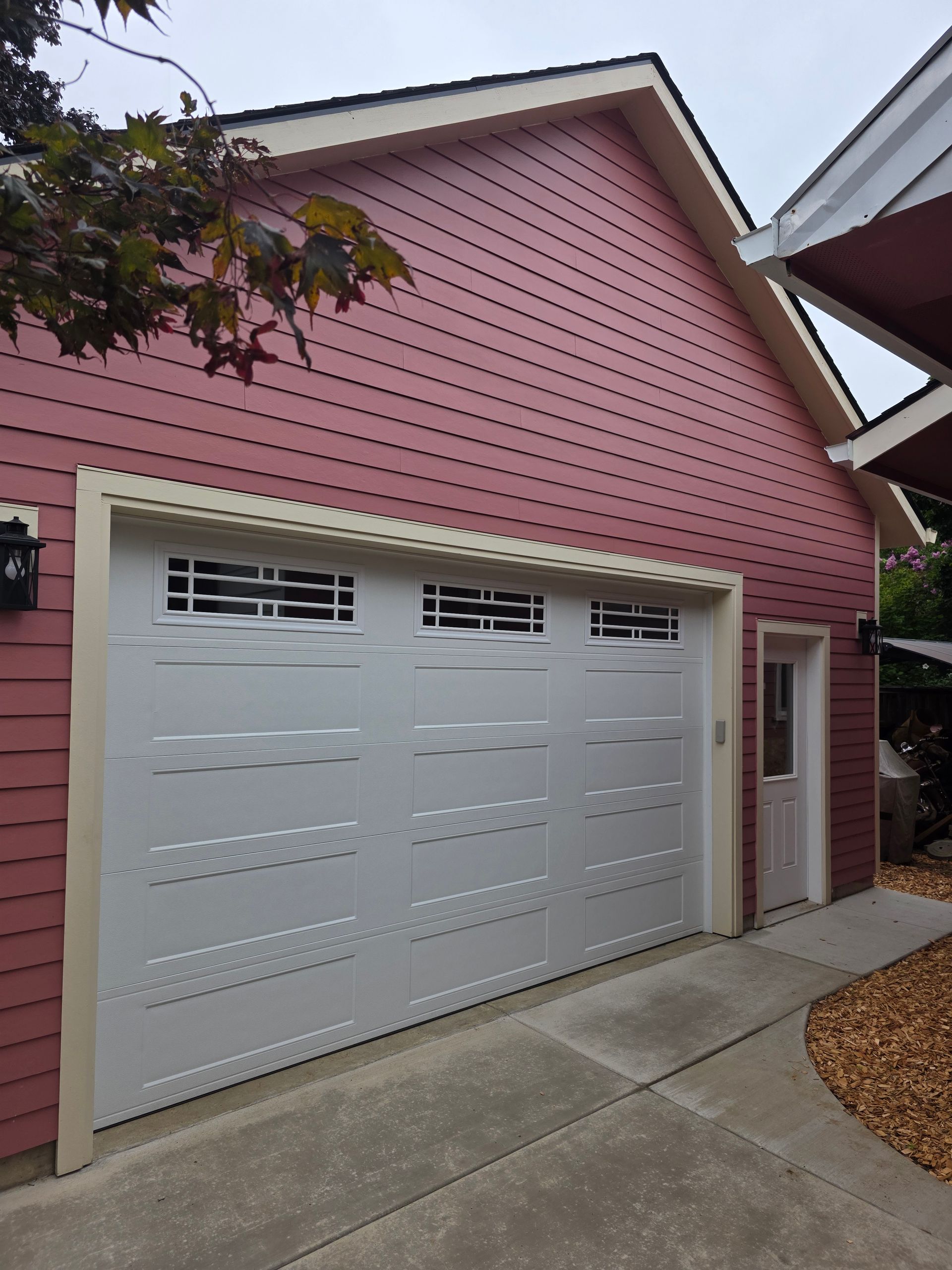 Pink house exterior with white double garage doors and a concrete driveway