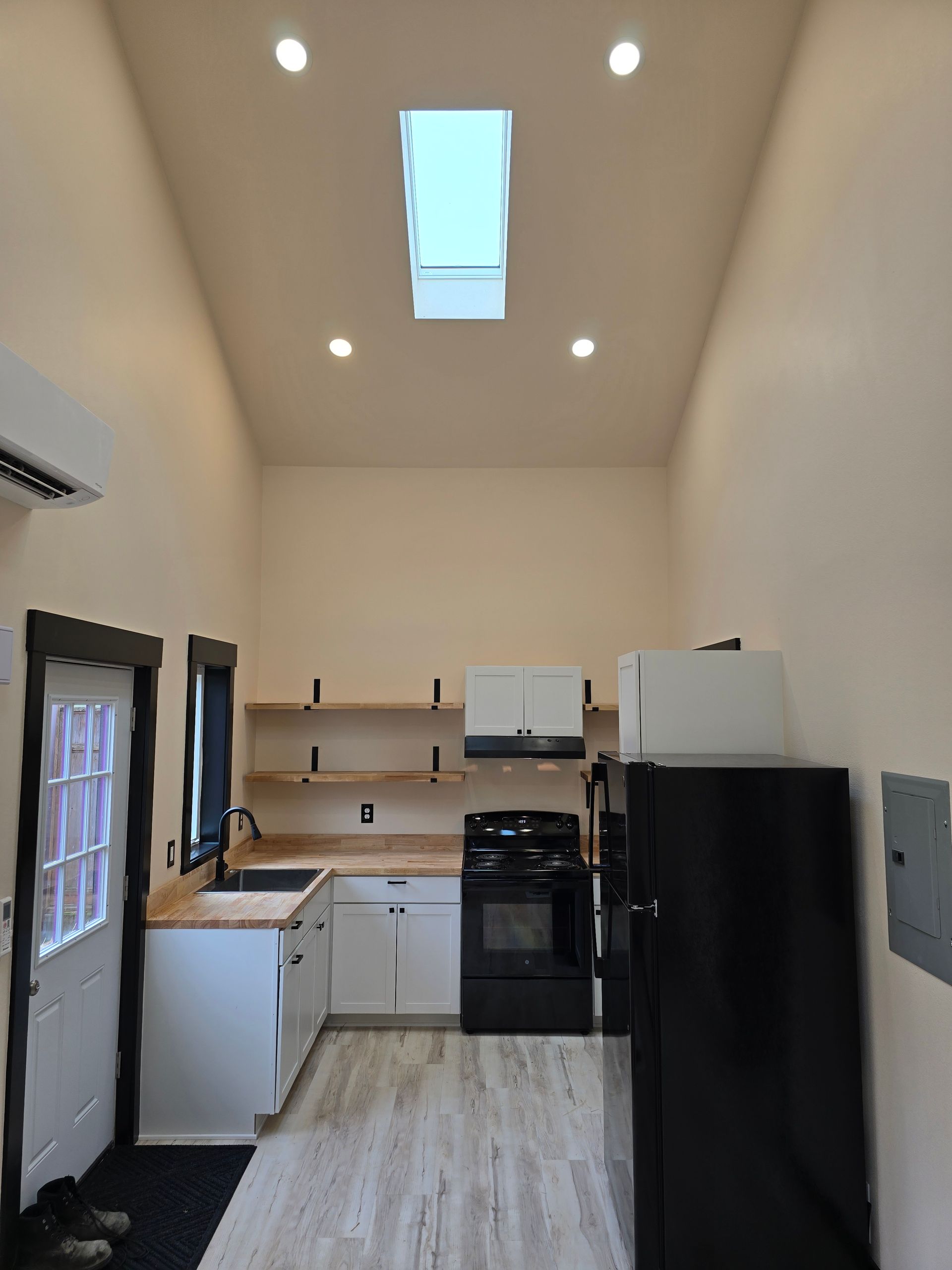Small modern kitchen with white cabinets, black appliances, wood counters, and a skylight ceiling