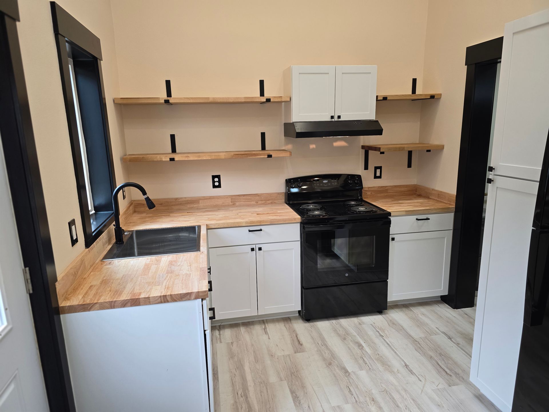 Small kitchen with black appliances, wood countertops, white cabinets, and open shelves.